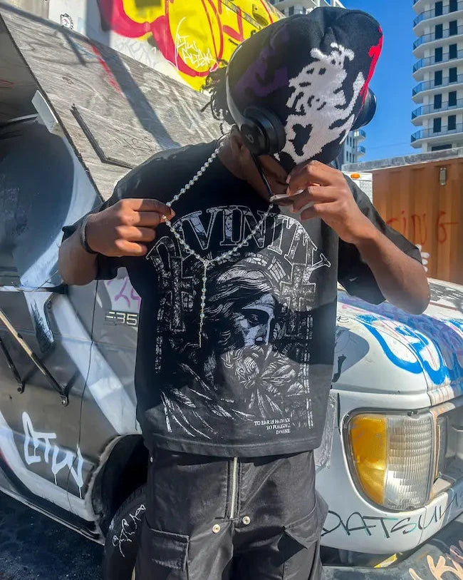 Person wearing a black t-shirt with a graphic design, standing in front of a vehicle with graffiti.
