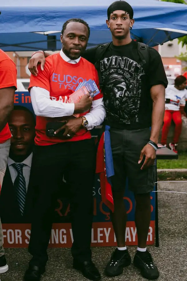 Two men standing together with a third man in the background, holding a blue object.